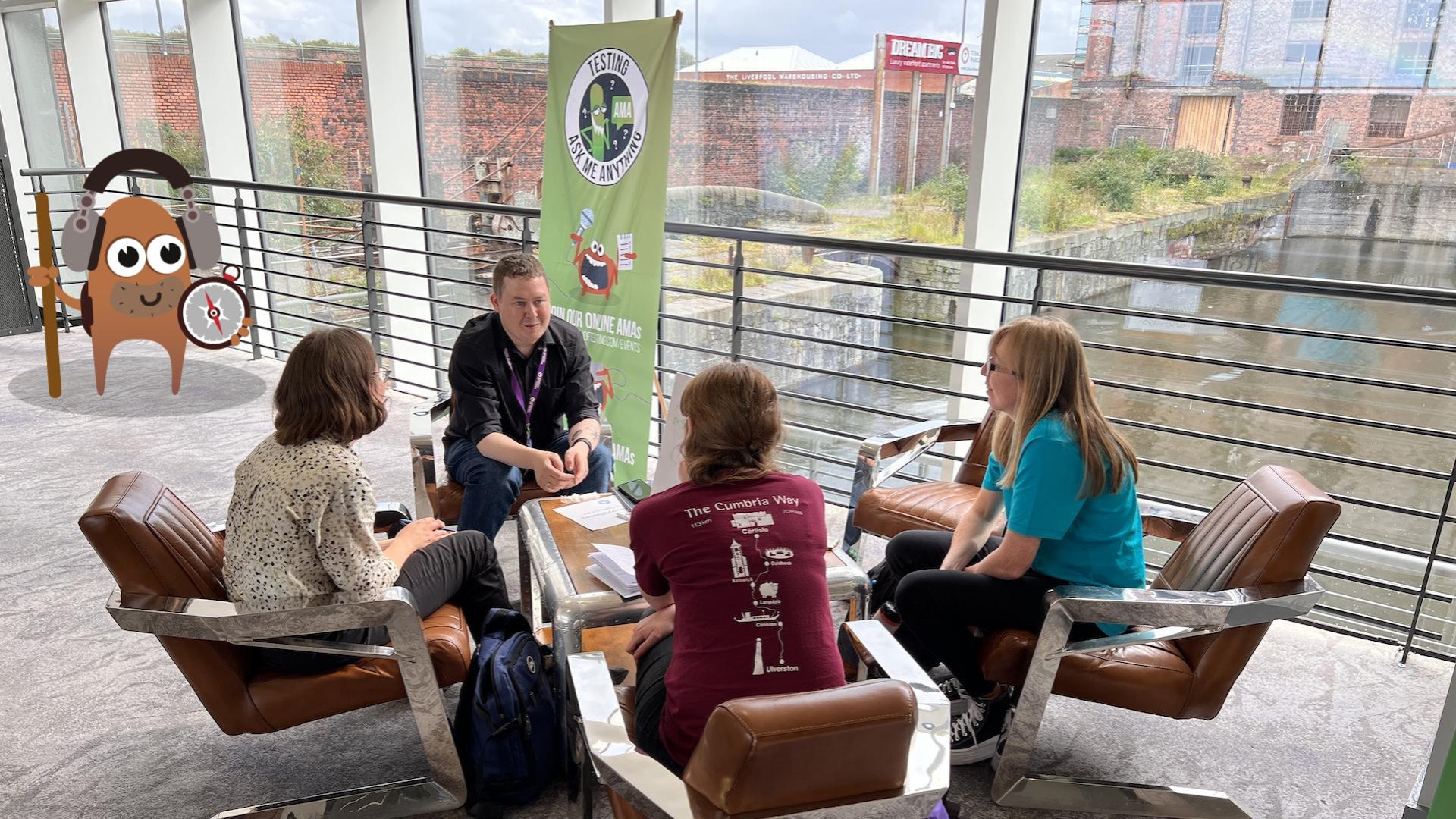 Four people stat on retro chairs gathered around a small coffee table at an event called TestBash. There is a brown smiling explorer monster character in the background.