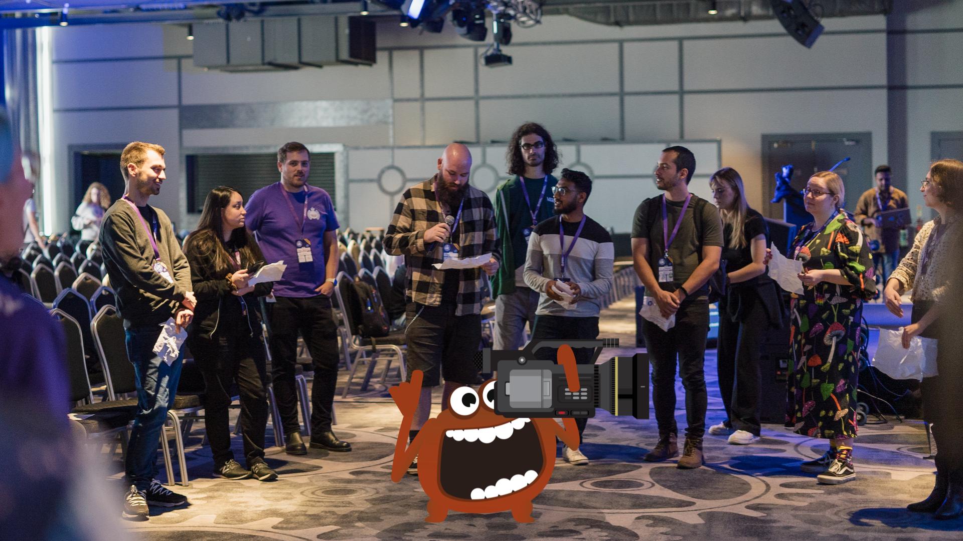 A row of people standing having a discussion at a TestBash software testing conference. There is a MoT monster character holding a video camera.