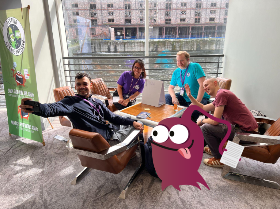 A group of four people and a monster character sat around a table posing for a selfie