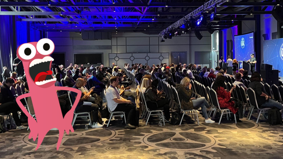 A big crowd of people listening to a talk at a conference. There is a monster illustration. 