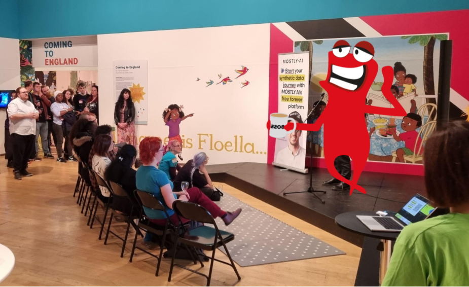 Several people gathered looking at a small stage. There is a red monster character with a mug in its hand. 