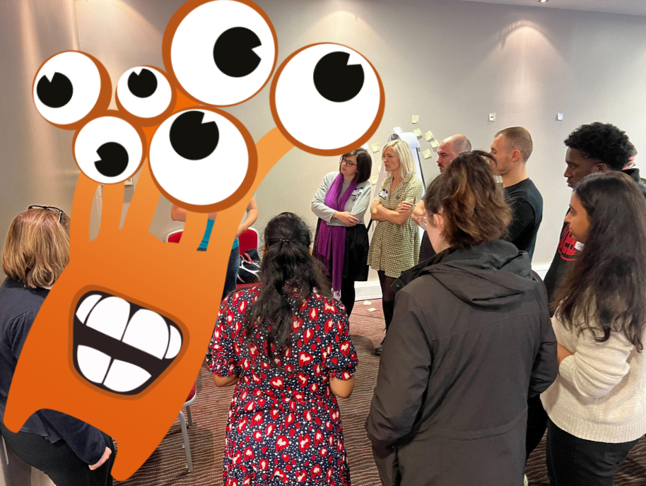 Several people standing in a circle. There is an orange monster with several eyes photobombing from the left. 